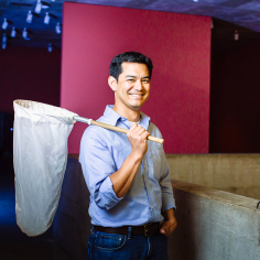 Neil Tsutsui standing in Woo Fai Han Hall with net draped over his back