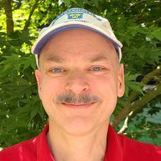 headshot of John Kubiatowicz taken outside, wearing a cap
