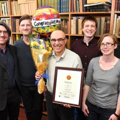 Robert Sharf standing with group of students in library, holding a plague and flowers